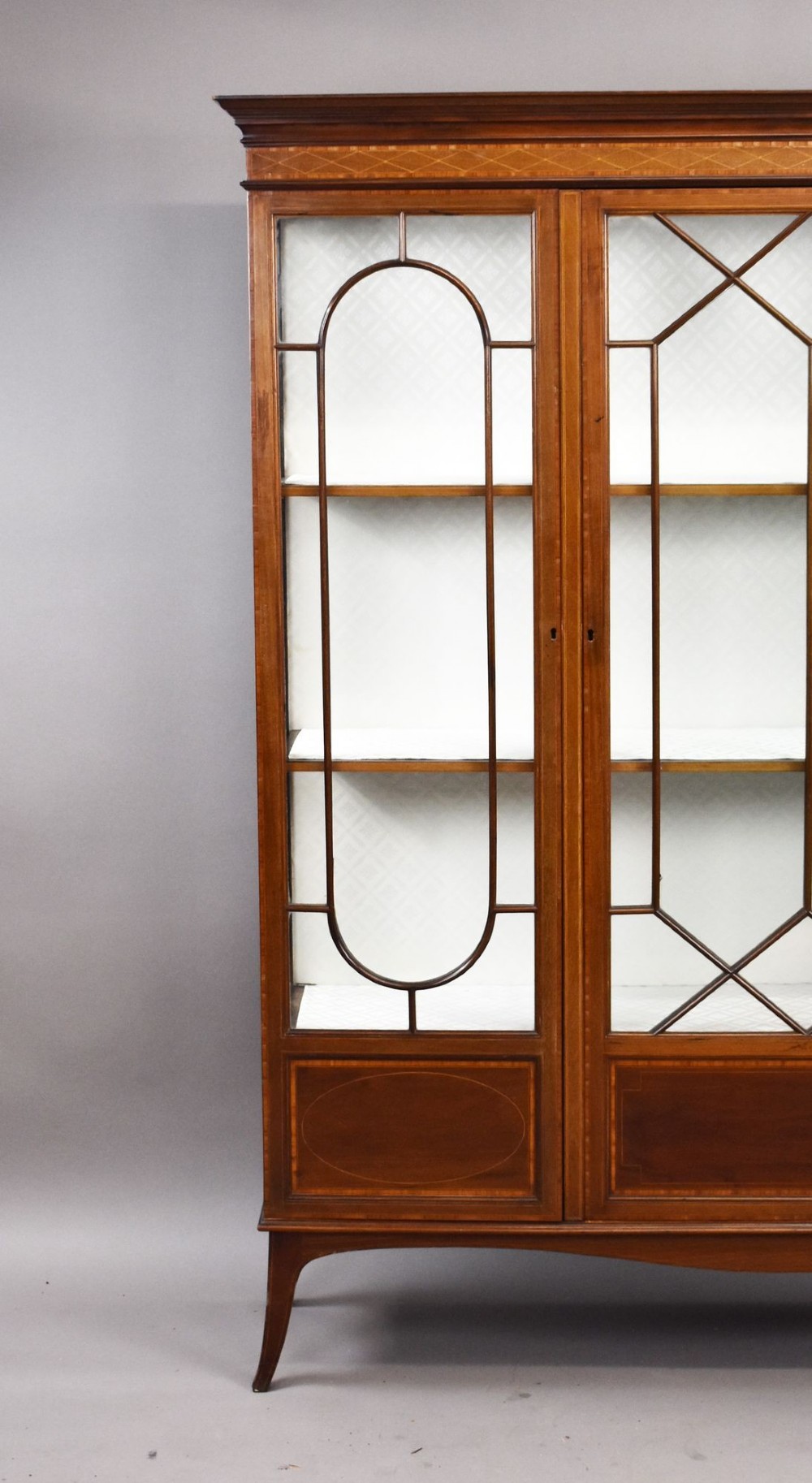An Edwardian mahogany display cabinet featuring three glazed doors with geometric astragal glazing bars, satinwood inlay panels, and tapered legs. View II