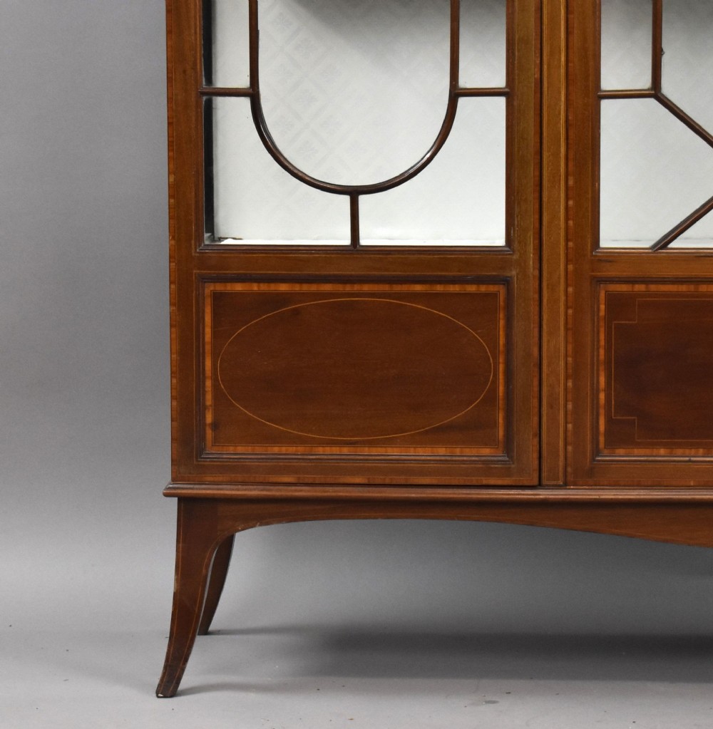 An Edwardian mahogany display cabinet featuring three glazed doors with geometric astragal glazing bars, satinwood inlay panels, and tapered legs. View V