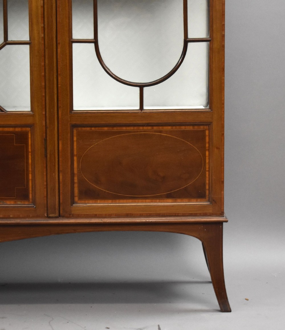 An Edwardian mahogany display cabinet featuring three glazed doors with geometric astragal glazing bars, satinwood inlay panels, and tapered legs. View VII