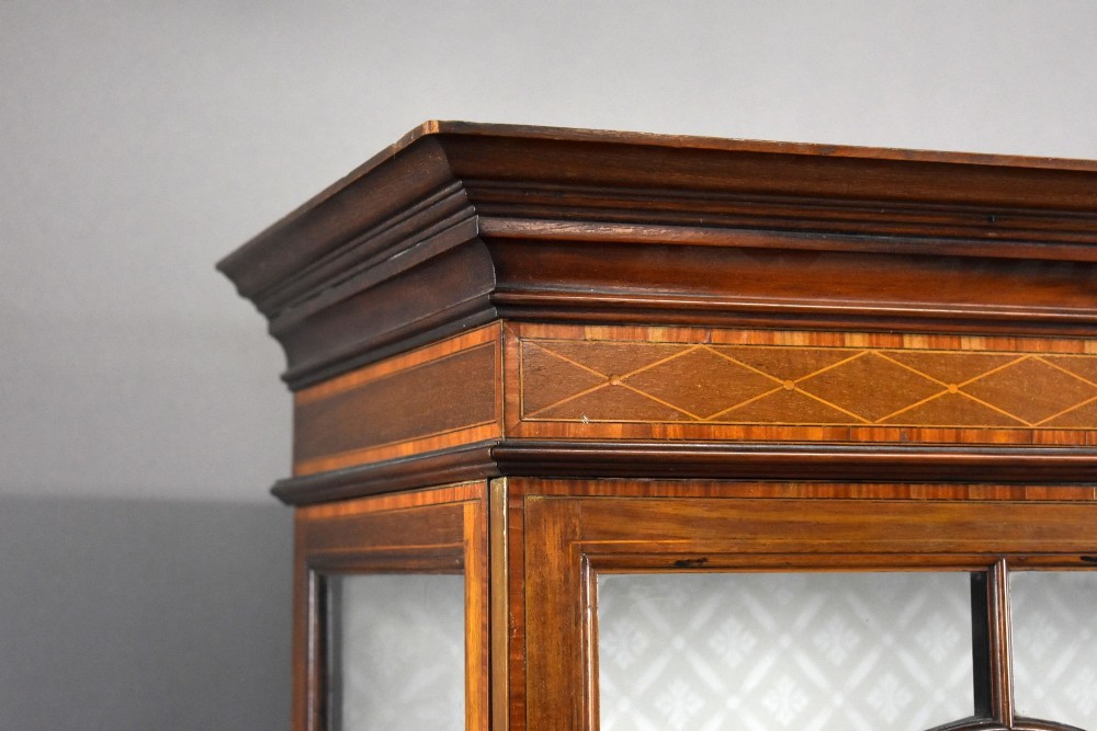 An Edwardian mahogany display cabinet featuring three glazed doors with geometric astragal glazing bars, satinwood inlay panels, and tapered legs. View VIII