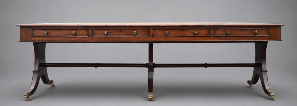 A large rectangular mahogany boardroom table with a leather inset top, accompanied by ten matching upholstered mahogany chairs resting on brass castor feet. View III