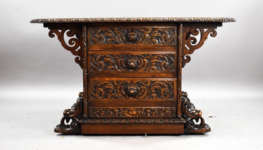 A dark oak Victorian writing desk featuring a green leather inset top with gold tooling, detailed lion mask carvings on the drawer fronts, and scroll corbels. View II