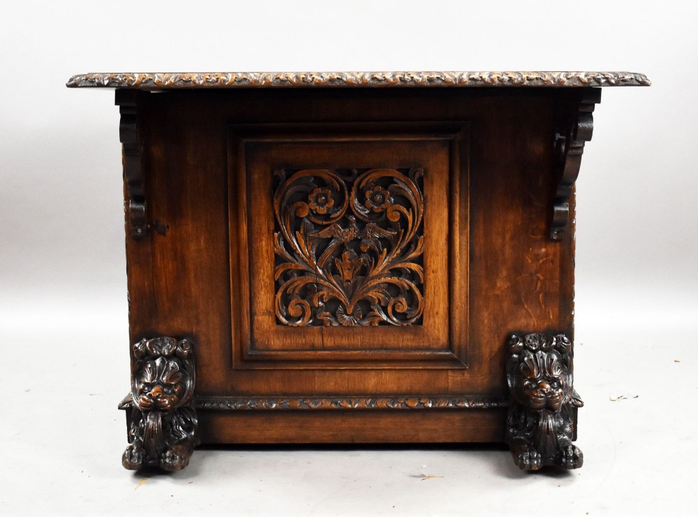 A dark oak Victorian writing desk featuring a green leather inset top with gold tooling, detailed lion mask carvings on the drawer fronts, and scroll corbels. View III