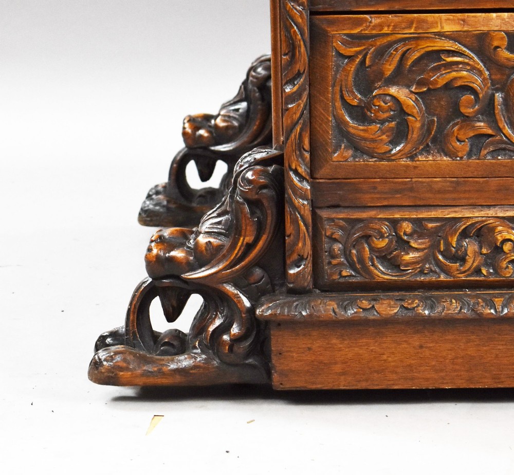 A dark oak Victorian writing desk featuring a green leather inset top with gold tooling, detailed lion mask carvings on the drawer fronts, and scroll corbels. View VI