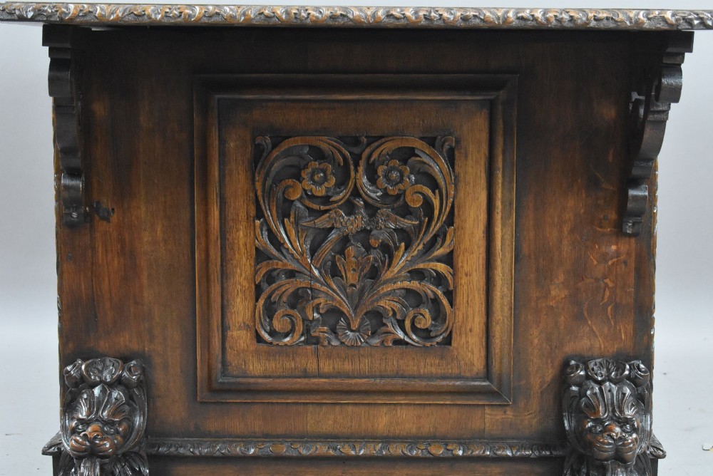 A dark oak Victorian writing desk featuring a green leather inset top with gold tooling, detailed lion mask carvings on the drawer fronts, and scroll corbels. View VIII