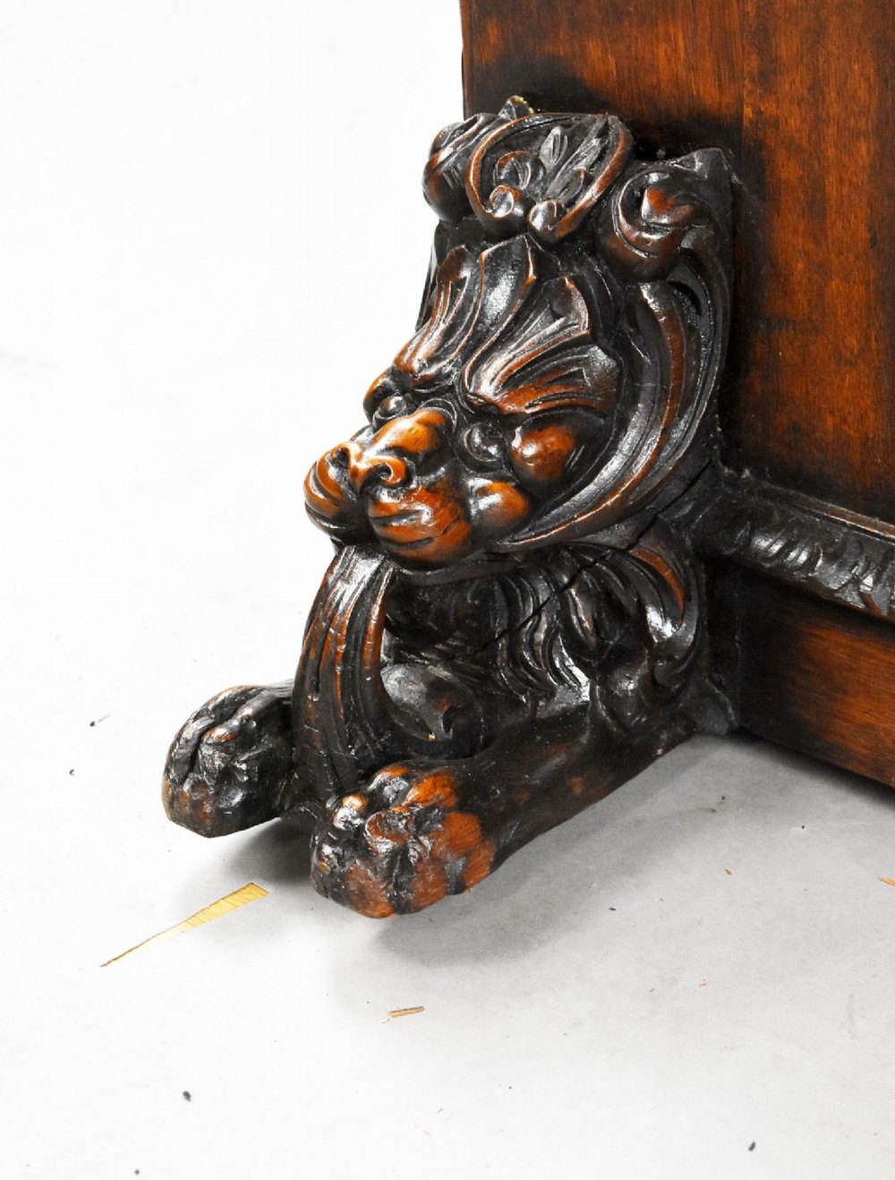 A dark oak Victorian writing desk featuring a green leather inset top with gold tooling, detailed lion mask carvings on the drawer fronts, and scroll corbels. View X