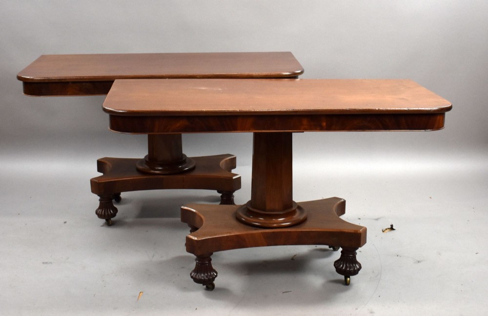 A pair of antique William IV mahogany console tables featuring rounded rectangular tops, central cylindrical pedestals, concave plinth bases, and carved lobed feet on brass castors. View II