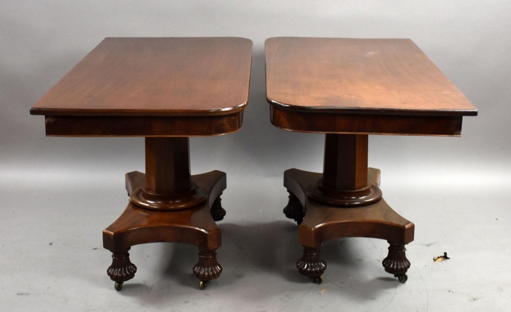 A pair of antique William IV mahogany console tables featuring rounded rectangular tops, central cylindrical pedestals, concave plinth bases, and carved lobed feet on brass castors. View IV