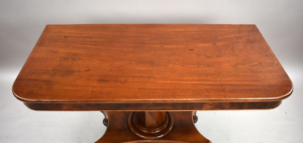 A pair of antique William IV mahogany console tables featuring rounded rectangular tops, central cylindrical pedestals, concave plinth bases, and carved lobed feet on brass castors. View V