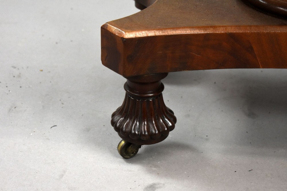 A pair of antique William IV mahogany console tables featuring rounded rectangular tops, central cylindrical pedestals, concave plinth bases, and carved lobed feet on brass castors. View VII
