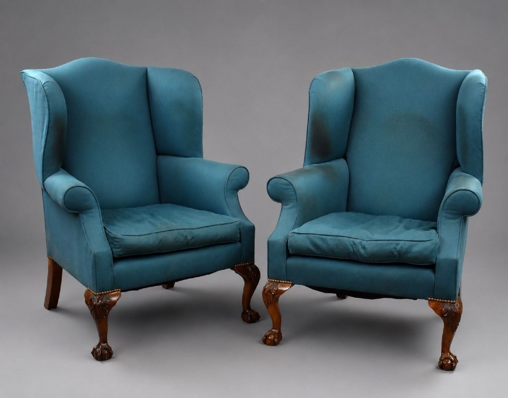 A pair of antique wingback armchairs upholstered in teal blue fabric with carved mahogany cabriole legs and claw-and-ball feet.