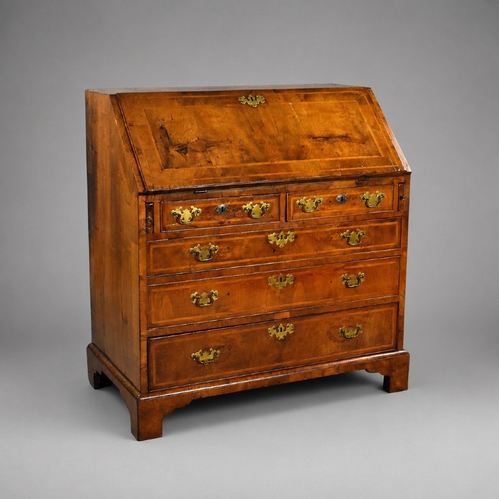 A George I figured walnut bureau with a sloping fall-front, brass drop handles, keyhole escutcheons, and bracket feet.