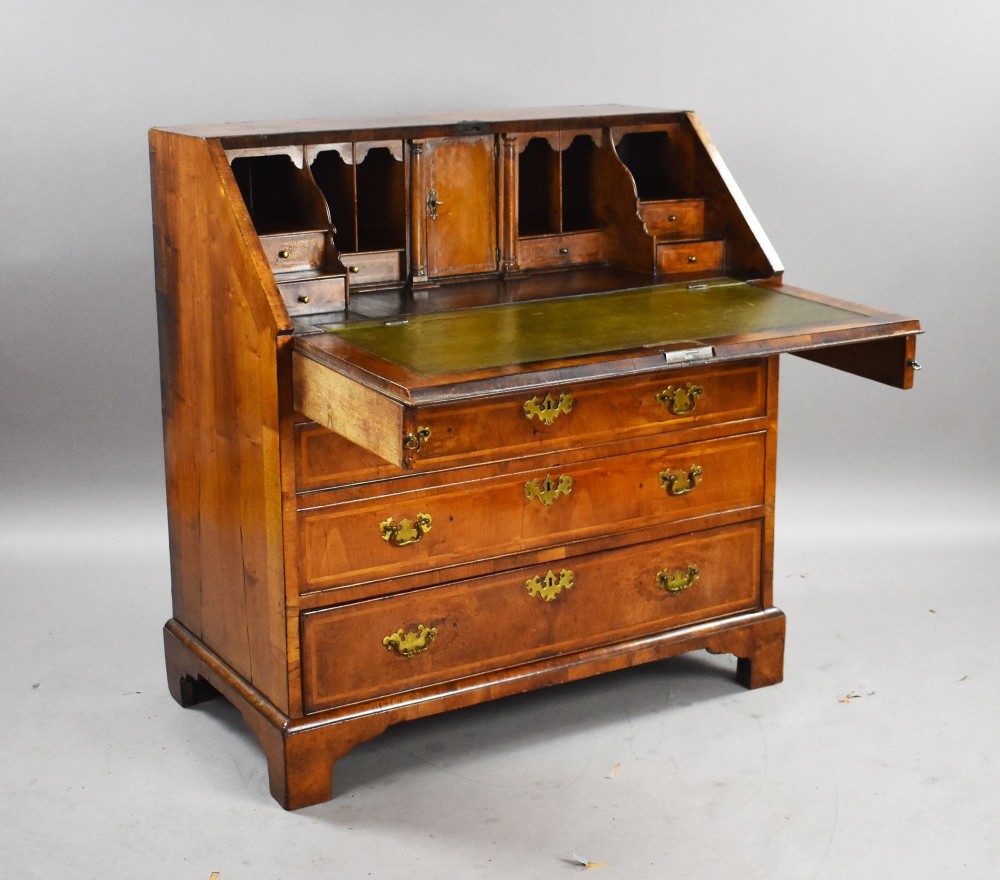 A George I figured walnut bureau with a sloping fall-front, brass drop handles, keyhole escutcheons, and bracket feet. View II