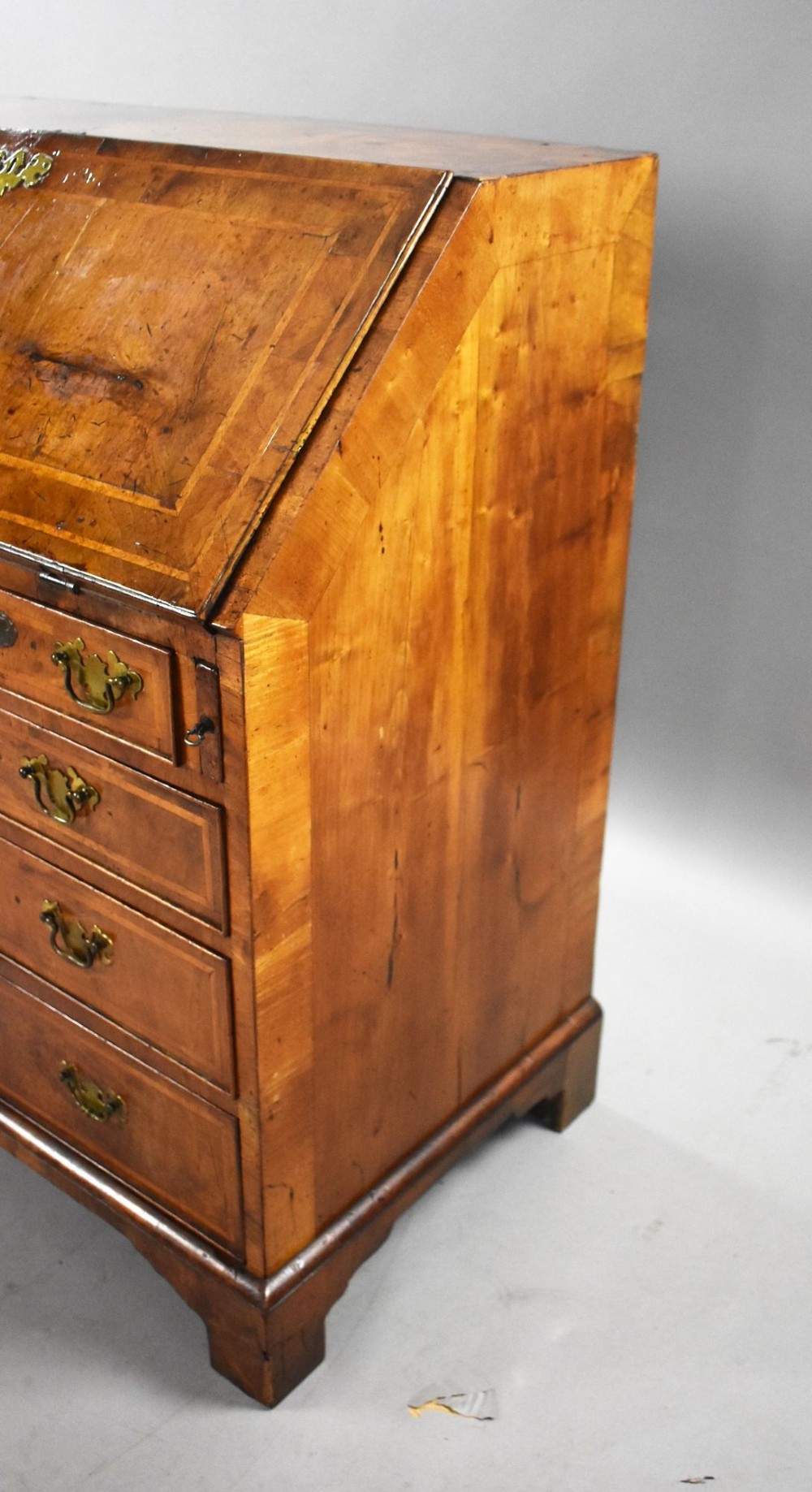 A George I figured walnut bureau with a sloping fall-front, brass drop handles, keyhole escutcheons, and bracket feet. View V