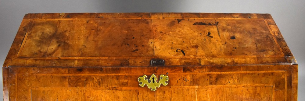 A George I figured walnut bureau with a sloping fall-front, brass drop handles, keyhole escutcheons, and bracket feet. View VI