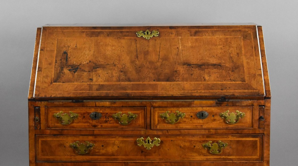 A George I figured walnut bureau with a sloping fall-front, brass drop handles, keyhole escutcheons, and bracket feet. View VII
