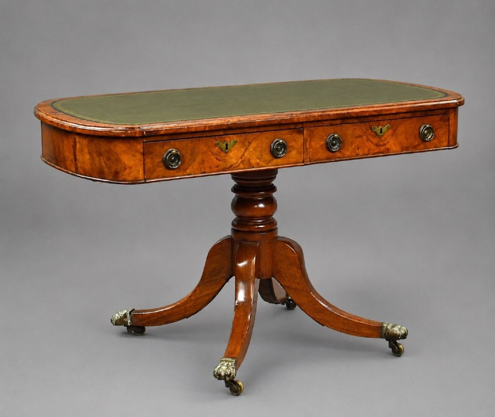 A Victorian burr walnut writing table featuring a green leather inset top, frieze drawers, and a central turned pedestal on splayed legs with brass lion paw castors.