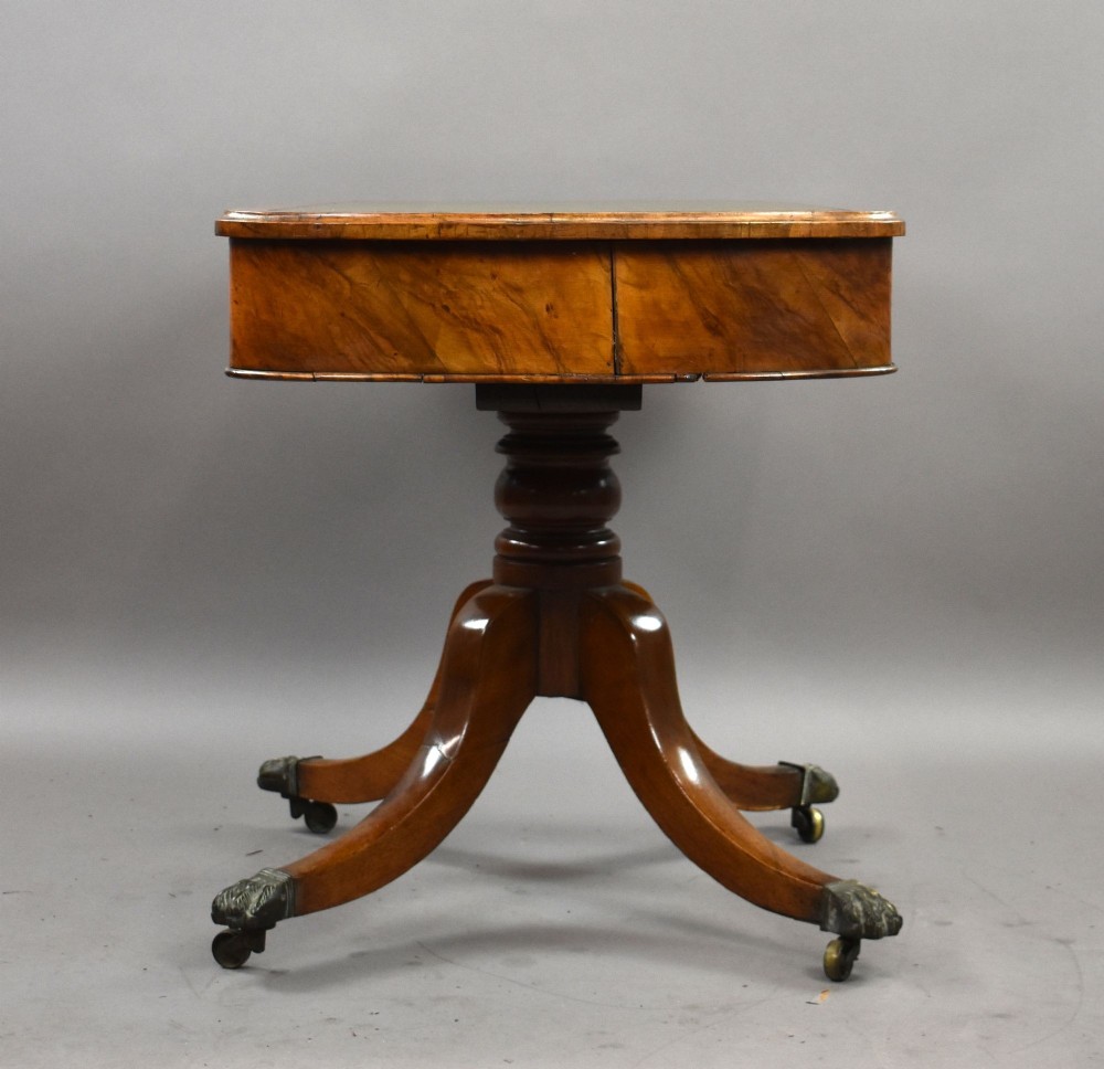 A Victorian burr walnut writing table featuring a green leather inset top, frieze drawers, and a central turned pedestal on splayed legs with brass lion paw castors. View V