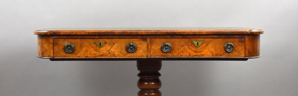 A Victorian burr walnut writing table featuring a green leather inset top, frieze drawers, and a central turned pedestal on splayed legs with brass lion paw castors. View VII