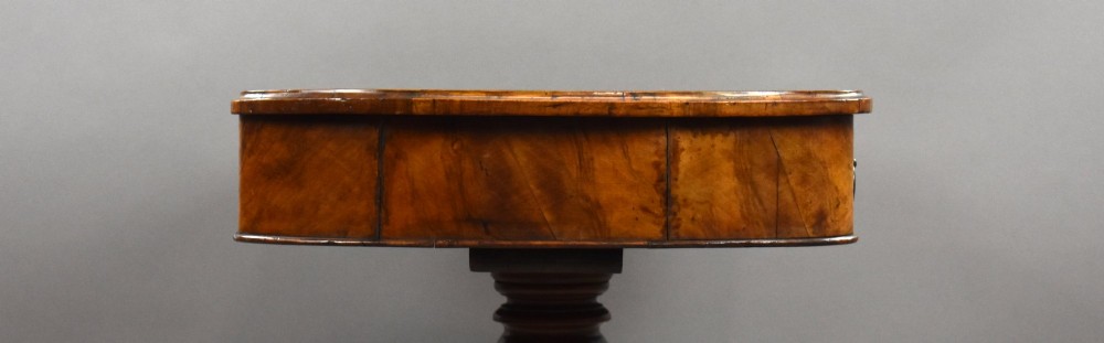 A Victorian burr walnut writing table featuring a green leather inset top, frieze drawers, and a central turned pedestal on splayed legs with brass lion paw castors. View IX