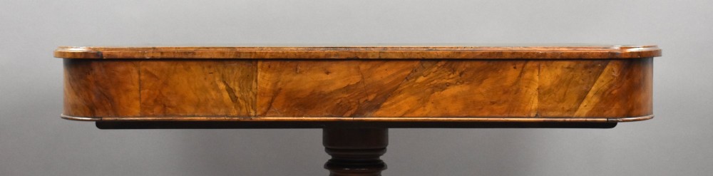 A Victorian burr walnut writing table featuring a green leather inset top, frieze drawers, and a central turned pedestal on splayed legs with brass lion paw castors. View X