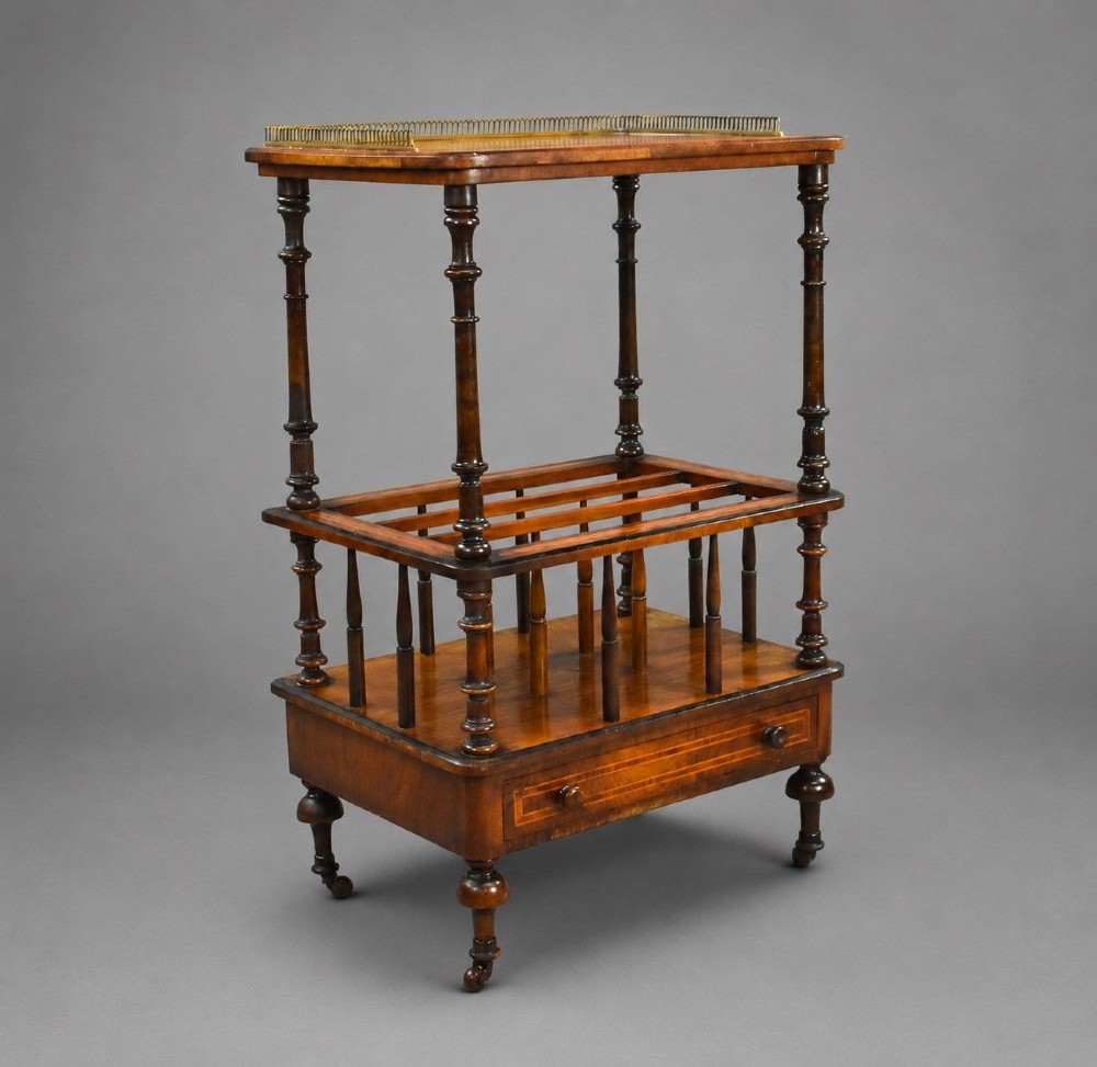 A Victorian burr walnut Canterbury featuring a top tier with a brass gallery rail, turned spindle columns, open partitions, a single inlaid drawer, and turned legs on brass castors.