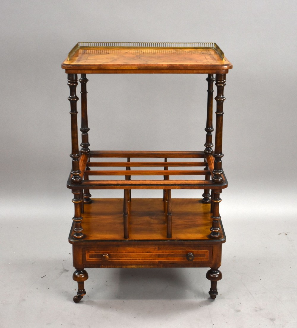 A Victorian burr walnut Canterbury featuring a top tier with a brass gallery rail, turned spindle columns, open partitions, a single inlaid drawer, and turned legs on brass castors. View II