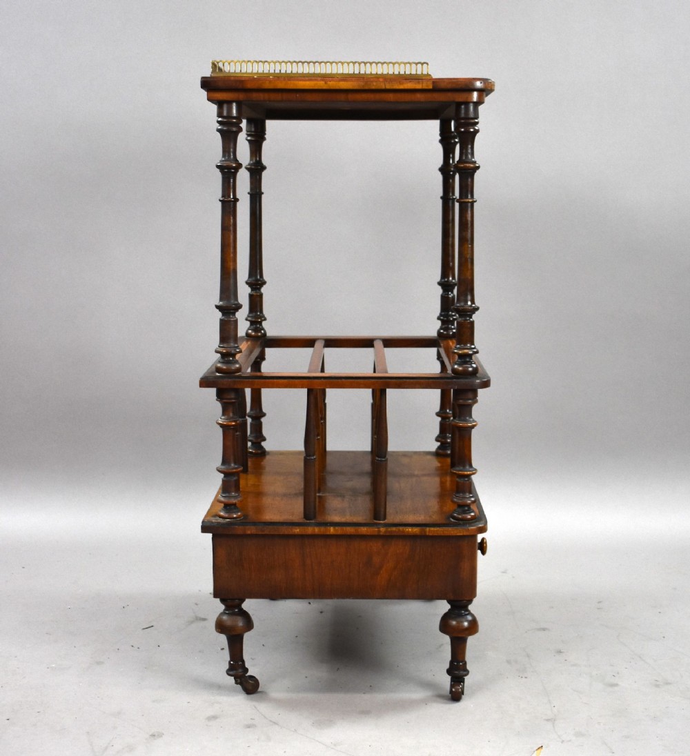 A Victorian burr walnut Canterbury featuring a top tier with a brass gallery rail, turned spindle columns, open partitions, a single inlaid drawer, and turned legs on brass castors. View III