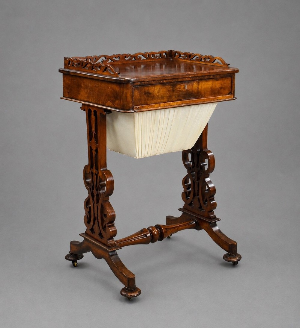 A Victorian mahogany work table featuring a fretwork gallery top, a single lockable drawer, a pleated cream fabric drop well, and carved scroll legs with brass castors.