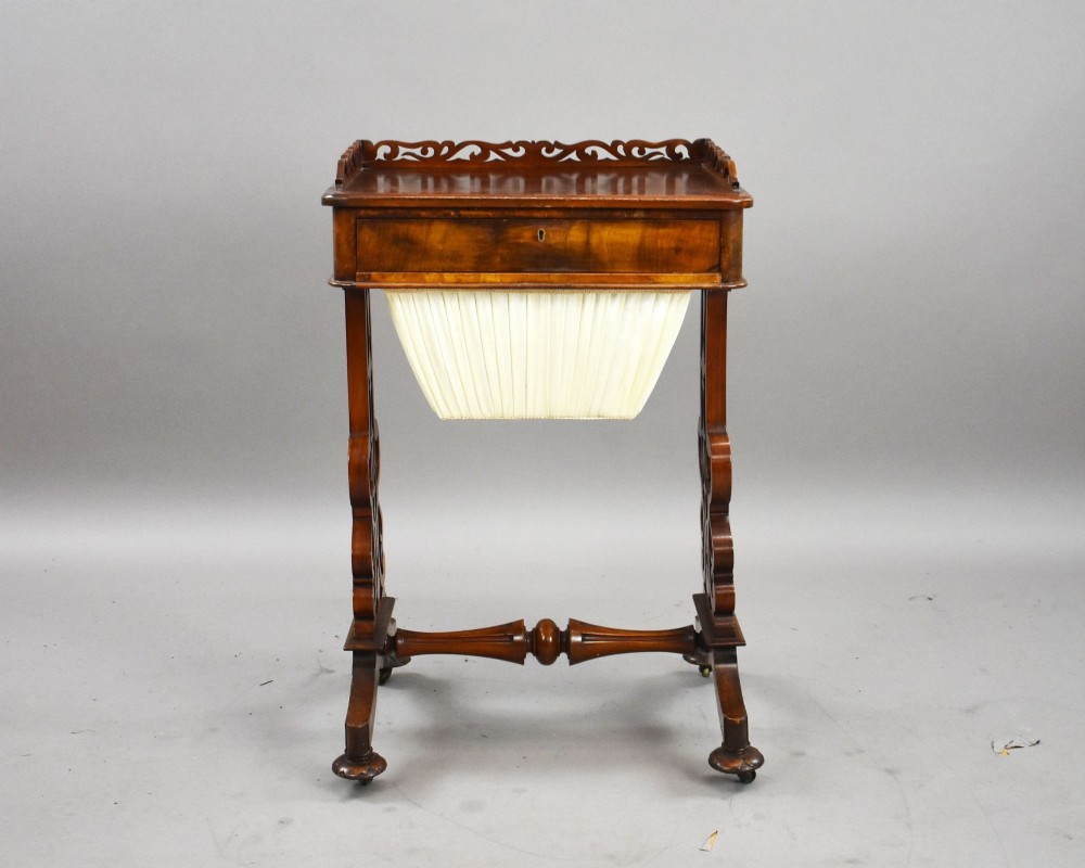 A Victorian mahogany work table featuring a fretwork gallery top, a single lockable drawer, a pleated cream fabric drop well, and carved scroll legs with brass castors. View II