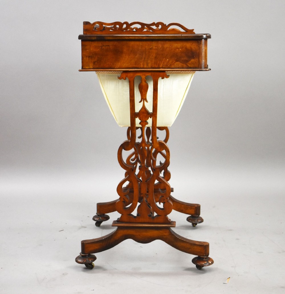 A Victorian mahogany work table featuring a fretwork gallery top, a single lockable drawer, a pleated cream fabric drop well, and carved scroll legs with brass castors. View III