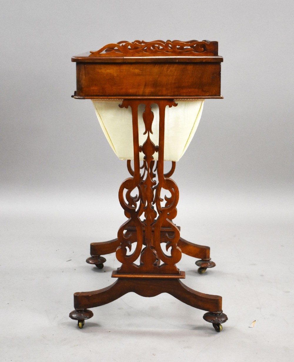 A Victorian mahogany work table featuring a fretwork gallery top, a single lockable drawer, a pleated cream fabric drop well, and carved scroll legs with brass castors. View IV
