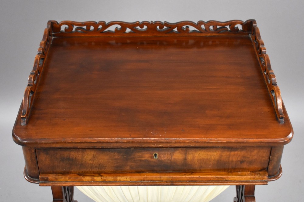 A Victorian mahogany work table featuring a fretwork gallery top, a single lockable drawer, a pleated cream fabric drop well, and carved scroll legs with brass castors. View V