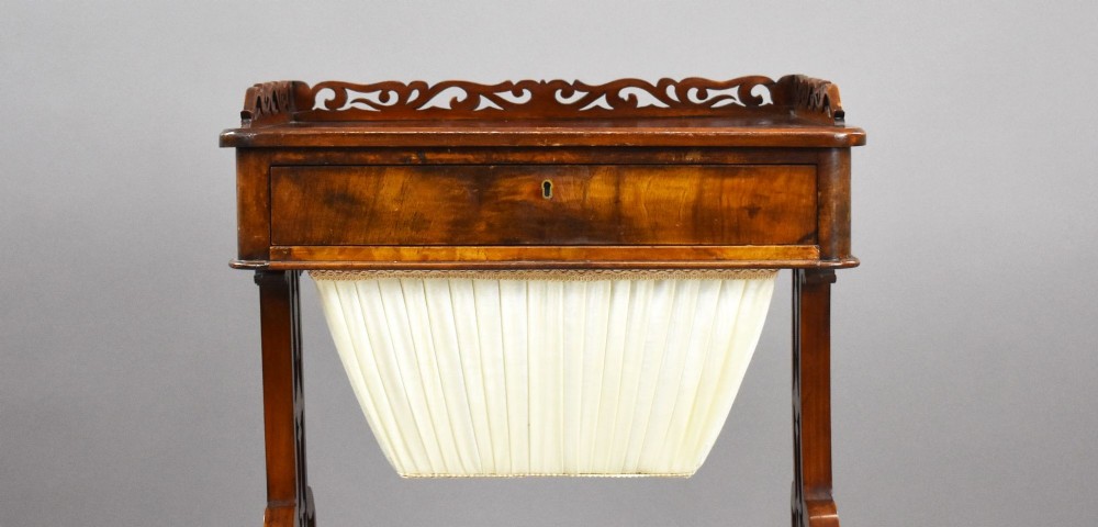 A Victorian mahogany work table featuring a fretwork gallery top, a single lockable drawer, a pleated cream fabric drop well, and carved scroll legs with brass castors. View VI