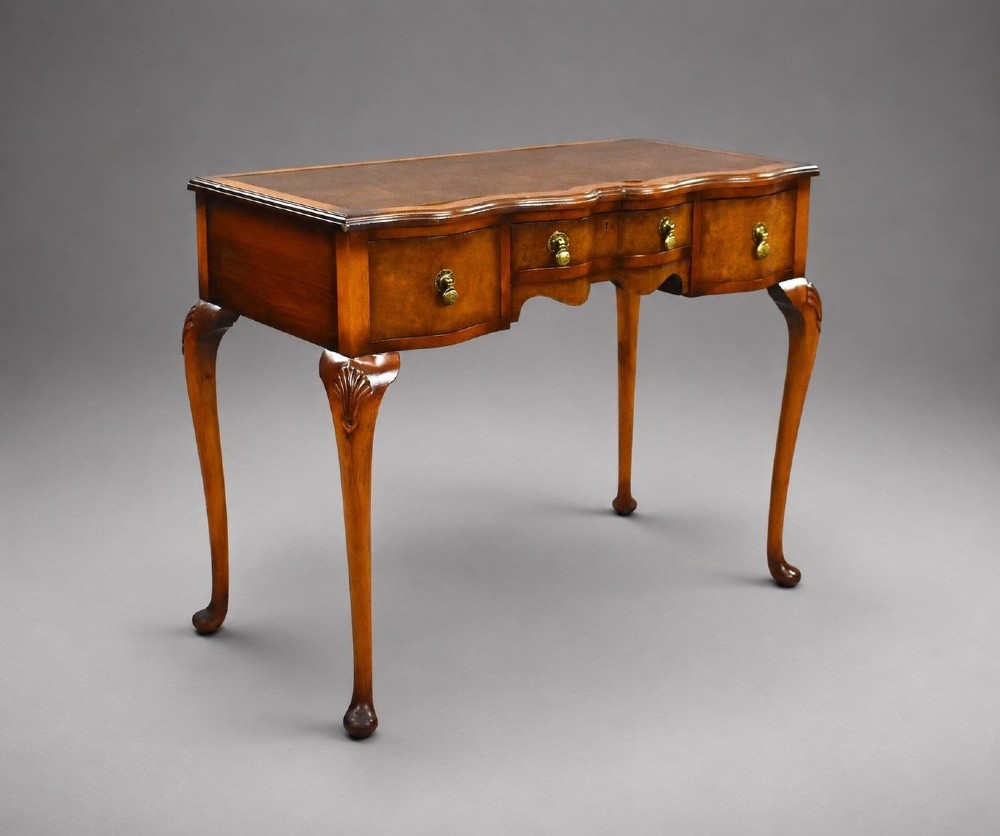 A Queen Anne style walnut writing desk featuring a brown leather inset top, serpentine front drawers with brass handles, and carved cabriole legs.