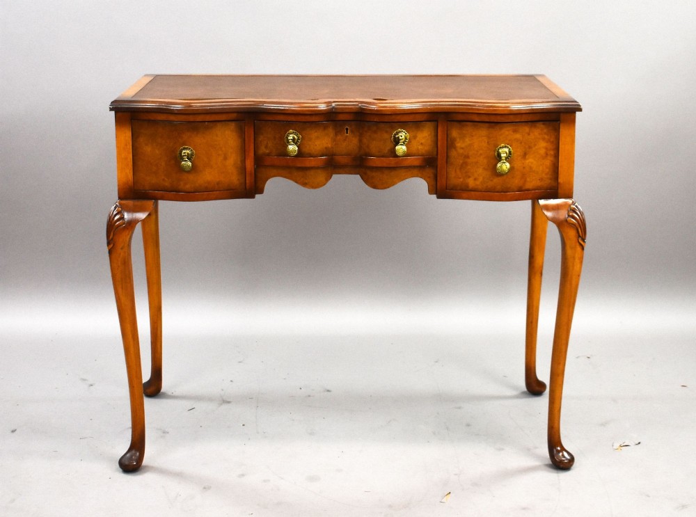 A Queen Anne style walnut writing desk featuring a brown leather inset top, serpentine front drawers with brass handles, and carved cabriole legs. View II