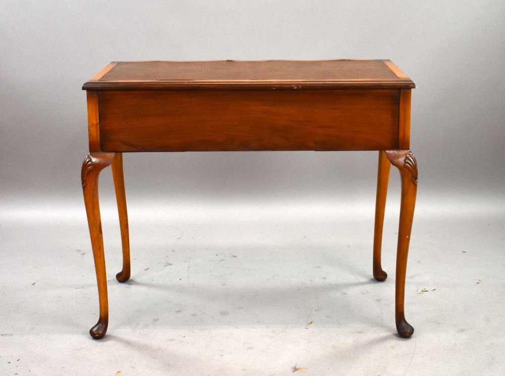 A Queen Anne style walnut writing desk featuring a brown leather inset top, serpentine front drawers with brass handles, and carved cabriole legs. View IV