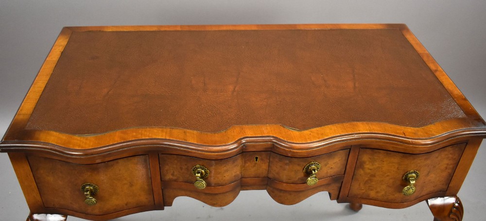 A Queen Anne style walnut writing desk featuring a brown leather inset top, serpentine front drawers with brass handles, and carved cabriole legs. View VII