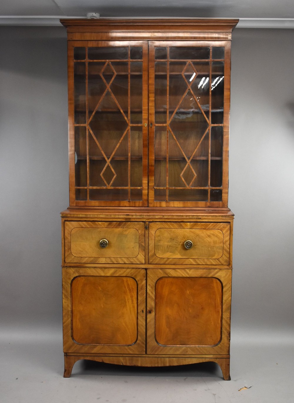 An antique mahogany secretaire bookcase featuring a glazed upper display cabinet with diamond astragal glazing bars above a lower chest and double cupboard base.
