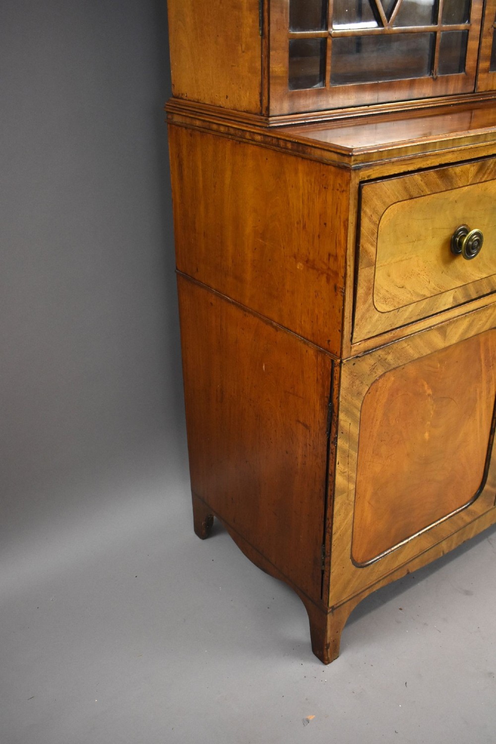 An antique mahogany secretaire bookcase featuring a glazed upper display cabinet with diamond astragal glazing bars above a lower chest and double cupboard base. View V