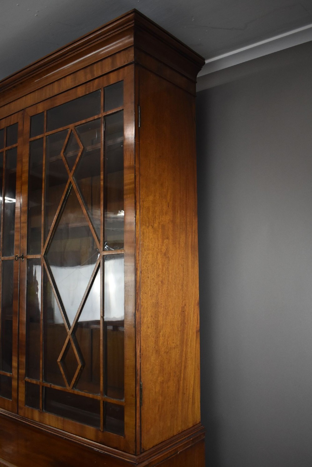 An antique mahogany secretaire bookcase featuring a glazed upper display cabinet with diamond astragal glazing bars above a lower chest and double cupboard base. View VI