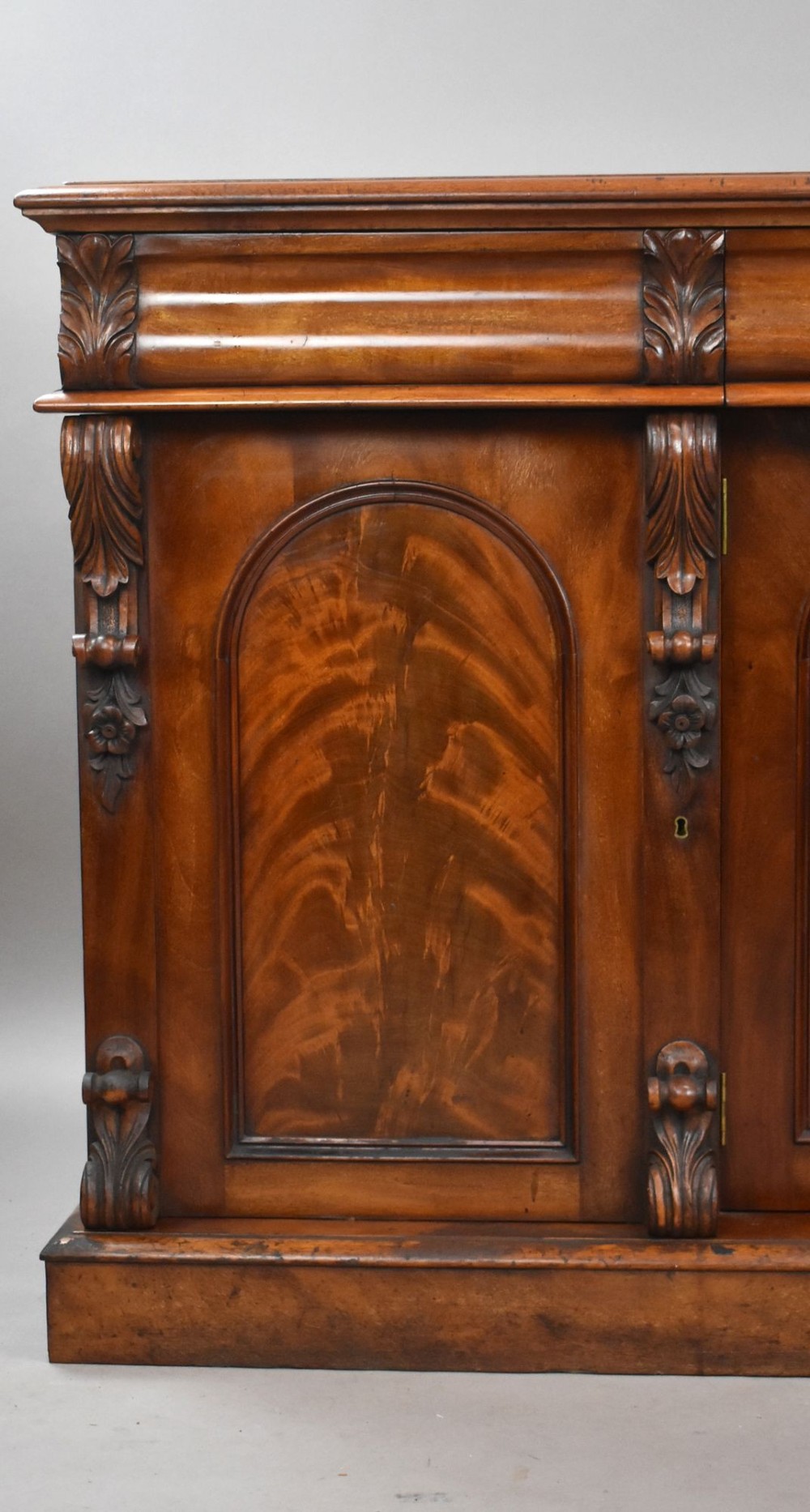 A nineteenth-century Victorian flame mahogany four-door sideboard featuring arched door panels, carved pilaster corbels, and a wide plinth base. View II