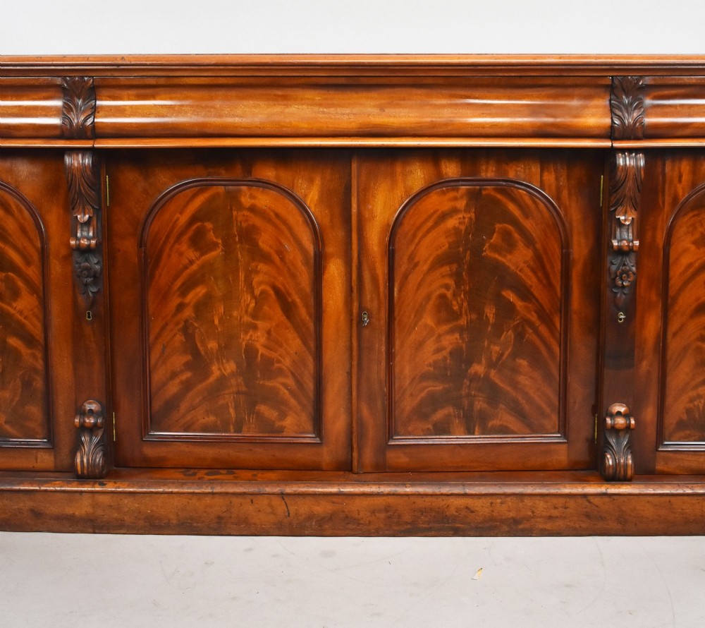 A nineteenth-century Victorian flame mahogany four-door sideboard featuring arched door panels, carved pilaster corbels, and a wide plinth base. View III
