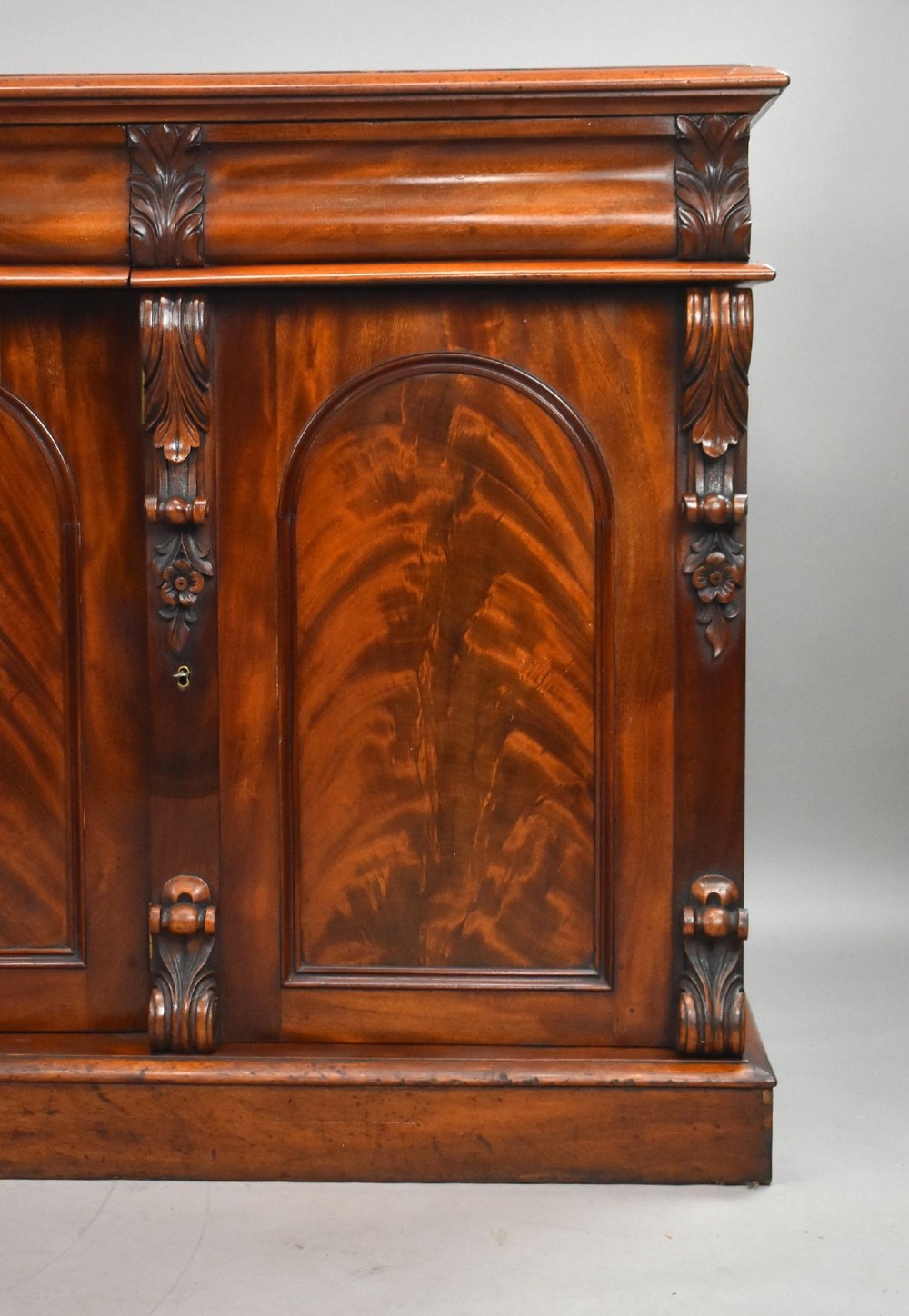 A nineteenth-century Victorian flame mahogany four-door sideboard featuring arched door panels, carved pilaster corbels, and a wide plinth base. View IV