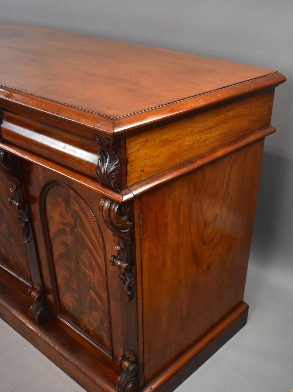 A nineteenth-century Victorian flame mahogany four-door sideboard featuring arched door panels, carved pilaster corbels, and a wide plinth base. View IX
