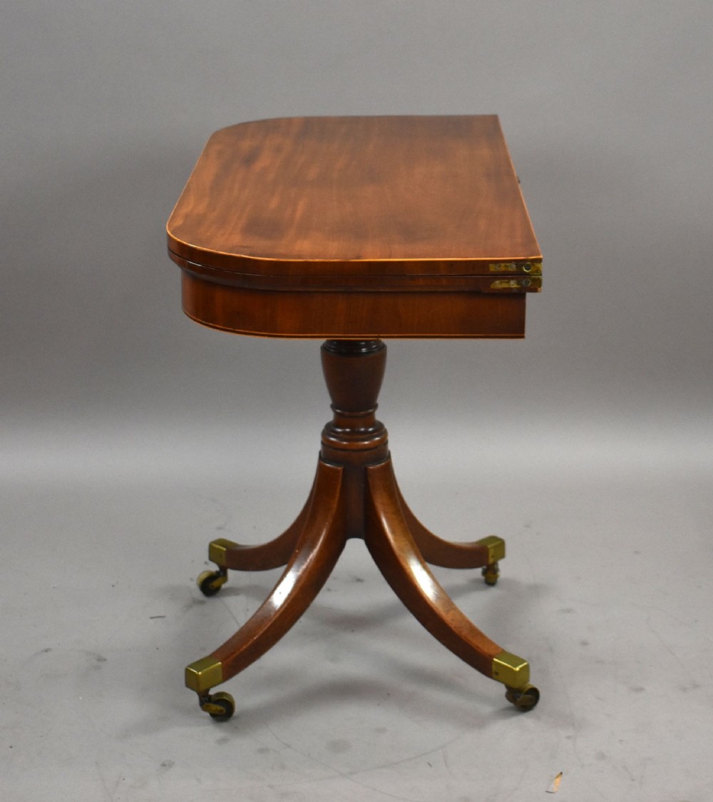 A Regency period mahogany fold-over card table featuring a rectangular swivel top, turned pedestal stem, and four splayed sabre legs fitted with brass castors. View VI