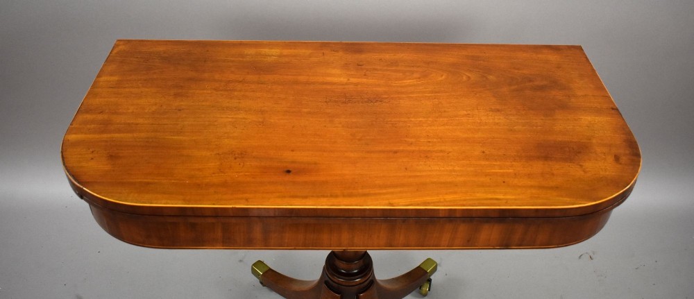 A Regency period mahogany fold-over card table featuring a rectangular swivel top, turned pedestal stem, and four splayed sabre legs fitted with brass castors. View VII