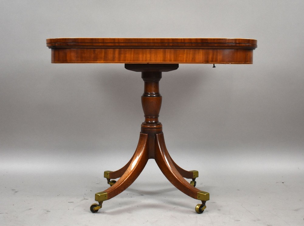 A Regency period mahogany fold-over card table featuring a rectangular swivel top, turned pedestal stem, and four splayed sabre legs fitted with brass castors. View VIII