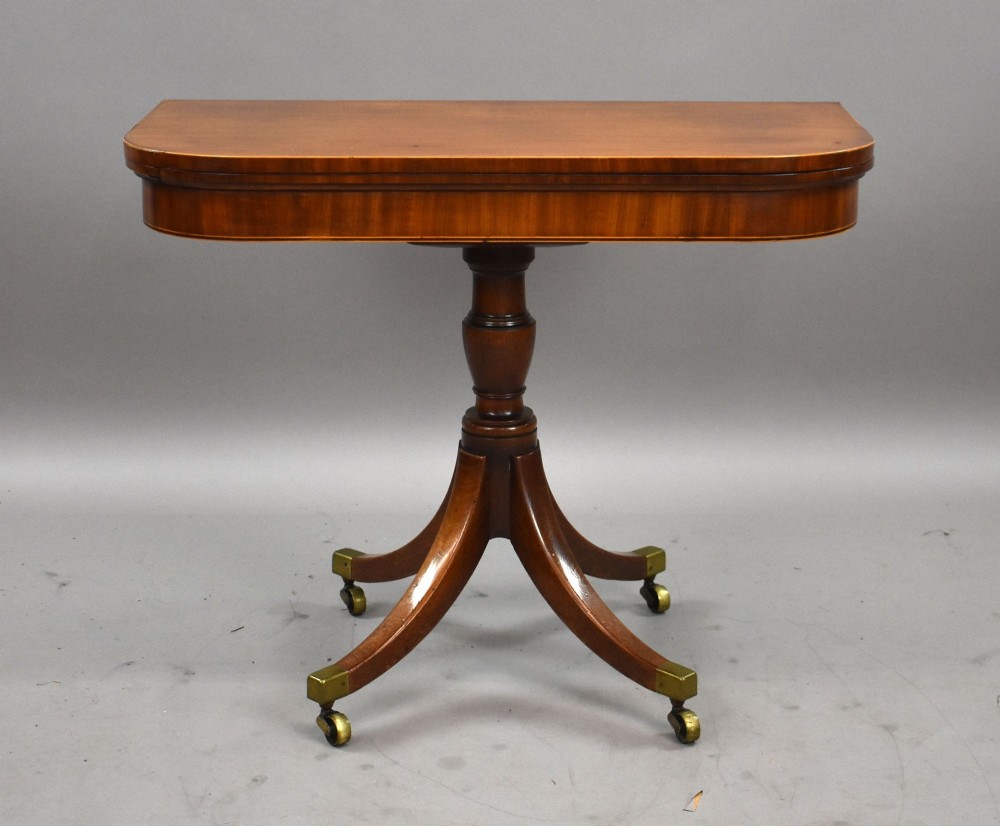 A Regency mahogany card table featuring a folding swivel top, a turned central pedestal column, and four splayed sabre legs with brass castors. View II