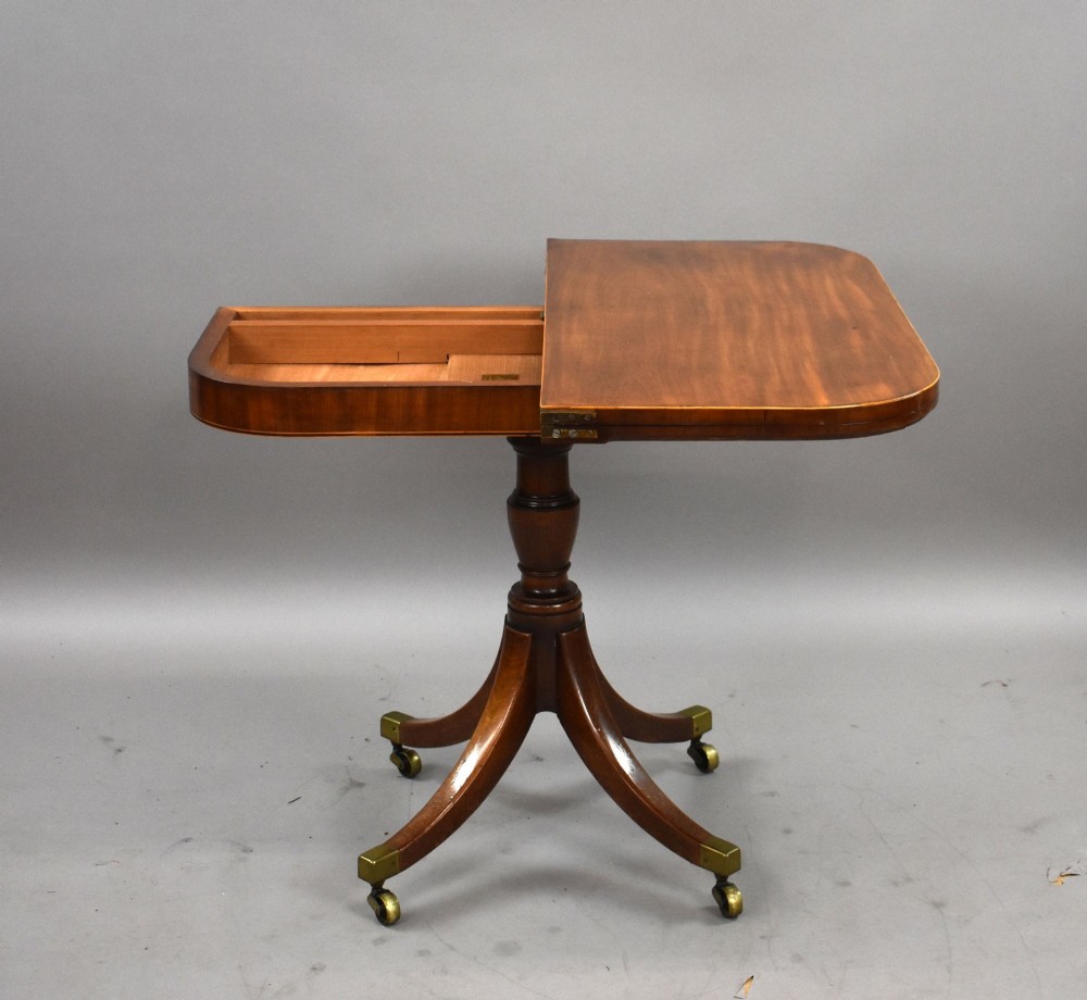 A Regency mahogany card table featuring a folding swivel top, a turned central pedestal column, and four splayed sabre legs with brass castors. View III